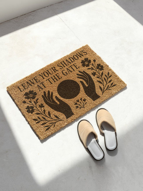 A rectangular, natural brown coir welcome mat with a textured surface, featuring an intricate, black witchy design intended for spiritual protection. The celestial and metaphysical pattern showcases a central manifestation spell circle with sacred geometry, radiating lines, and is accented with stars and crescent moons at the corners, creating a unique piece of entryway decor.